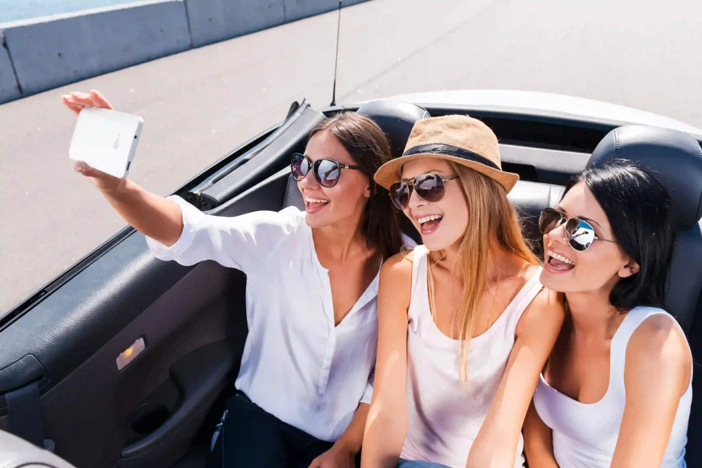 Young women in a convertible taking a selfie, related to boosting happiness.